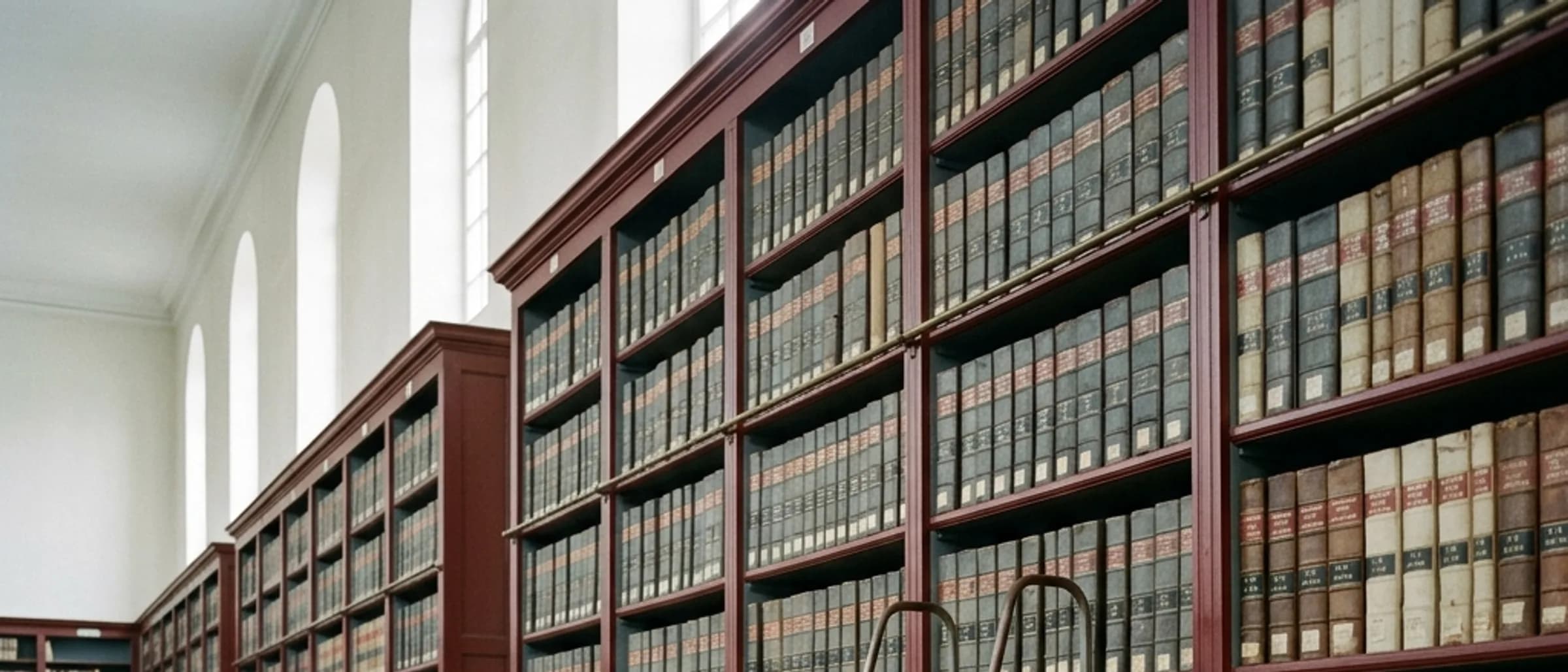 Shelves of bound records and a rolling ladder in an empty archives hall.